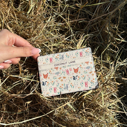 Hand holding Coconut Lane card holder with colorful animal prints, shown over dry grass in sunlight.