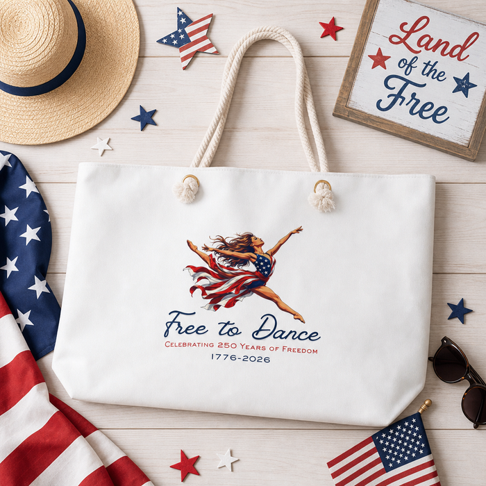 White tote bag with Free to Dance  Celebrating 250 Years of Freedom 1776-2026 design on a wooden surface with American flags and a hat.