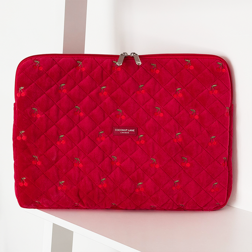 Bright red quilted velvet laptop sleeve with cherry pattern, displayed on a white shelf.